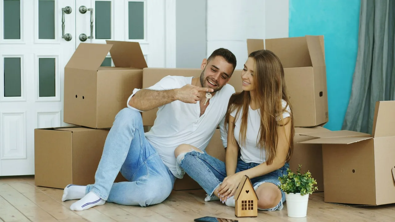 A couple sitting among moving boxes in their first home, holding house keys